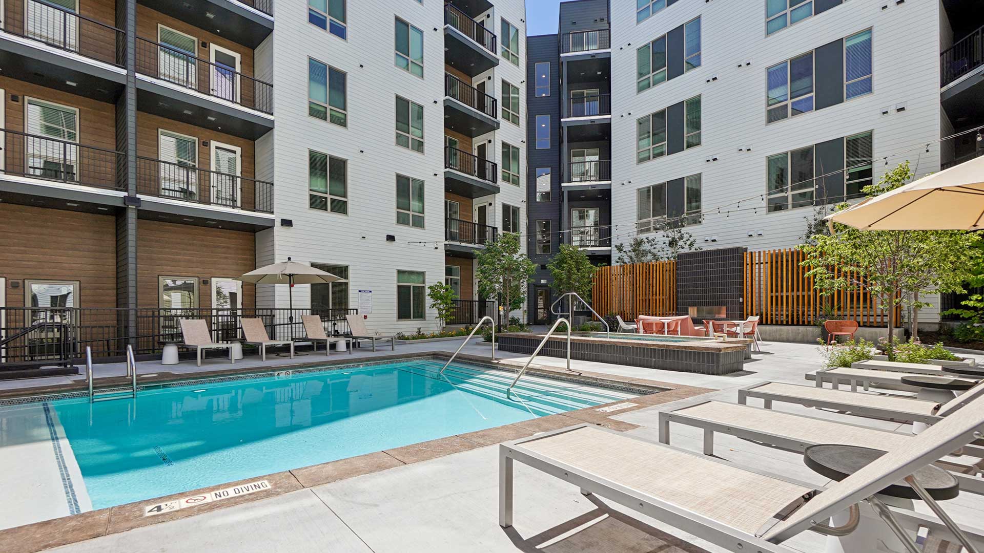 Outdoor swimming pool and spa area at Tempo at Nine Mile with modern lounge chairs, landscaped courtyard seating, and surrounding apartment balconies.