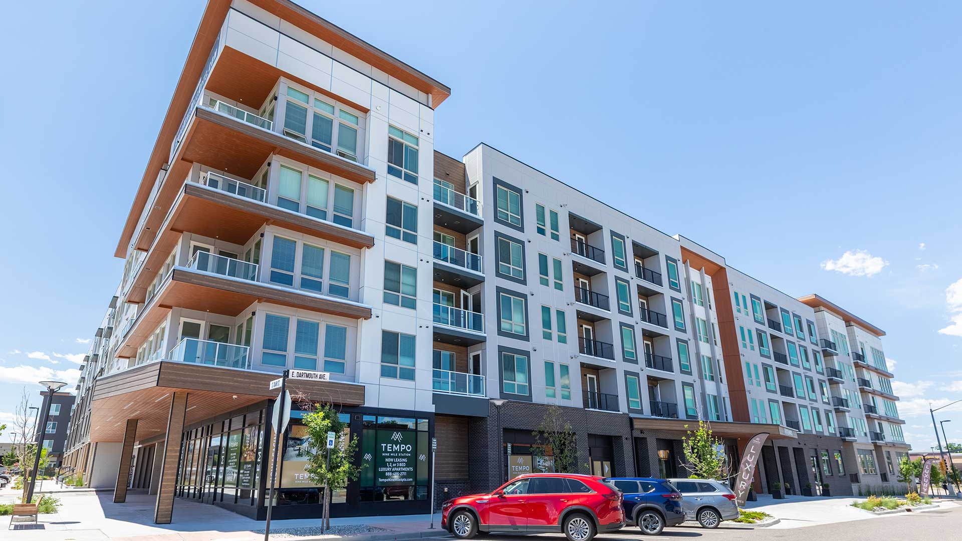 Exterior view of Tempo at Nine Mile apartment community featuring modern multi-story architecture, large balconies, storefront leasing office, and street-level parking.