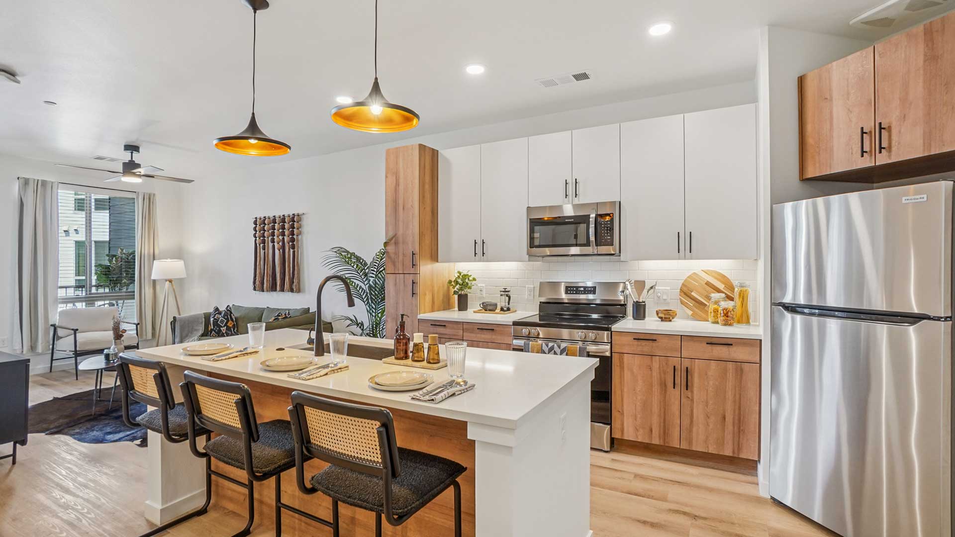 Modern apartment kitchen with large island, stainless steel appliances, quartz countertops, and open living area at Tempo at Nine Mile apartments.