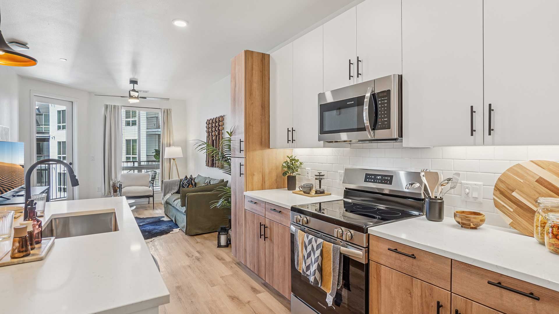 Modern apartment interior featuring a contemporary kitchen with stainless-steel appliances, quartz countertops, wood-tone cabinetry, and an open-concept living area with balcony access at Tempo at Nine Mile apartments.