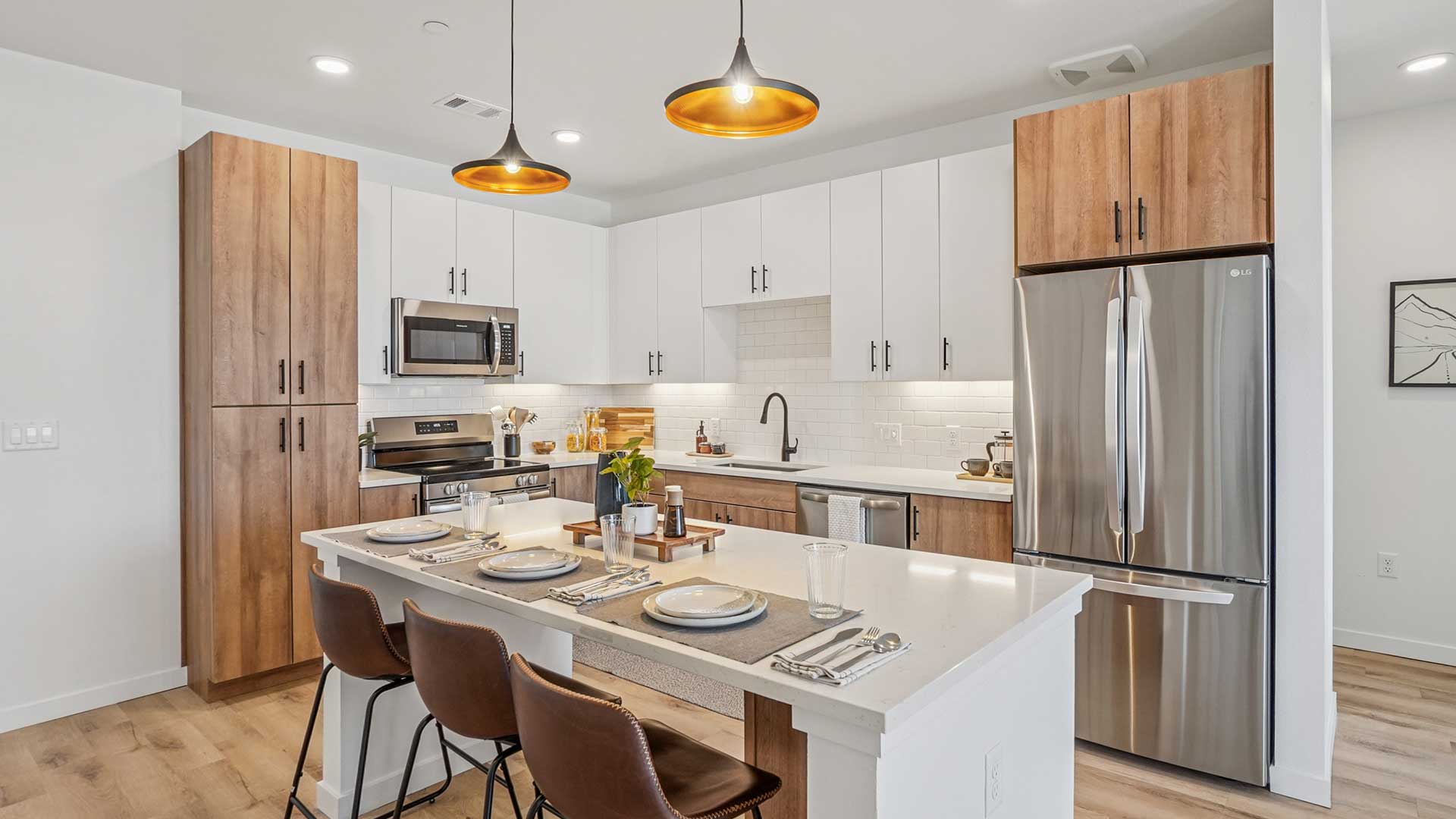 Modern apartment kitchen with stainless-steel appliances, large island seating, white cabinetry, and wood-style finishes at Tempo at Nine Mile.