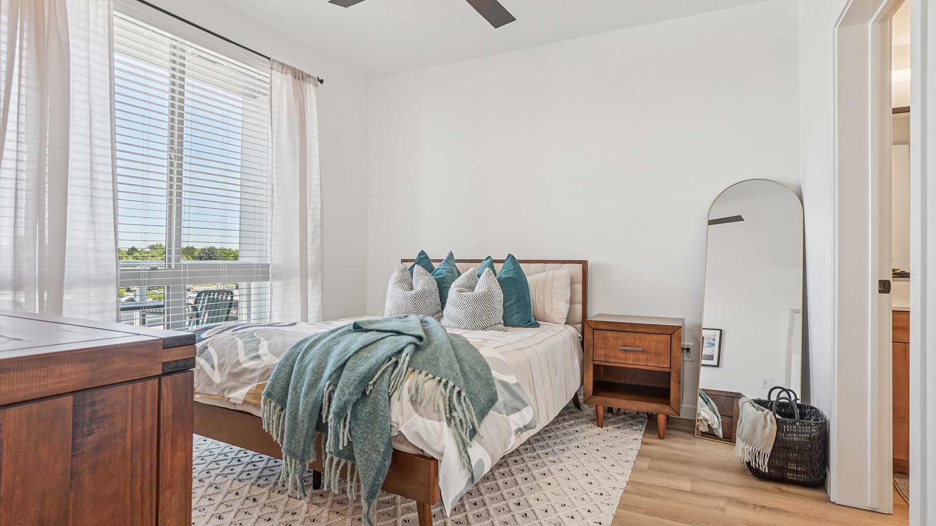 Modern apartment bedroom with large window, wood-style flooring, and contemporary finishes at Tempo at Nine Mile.