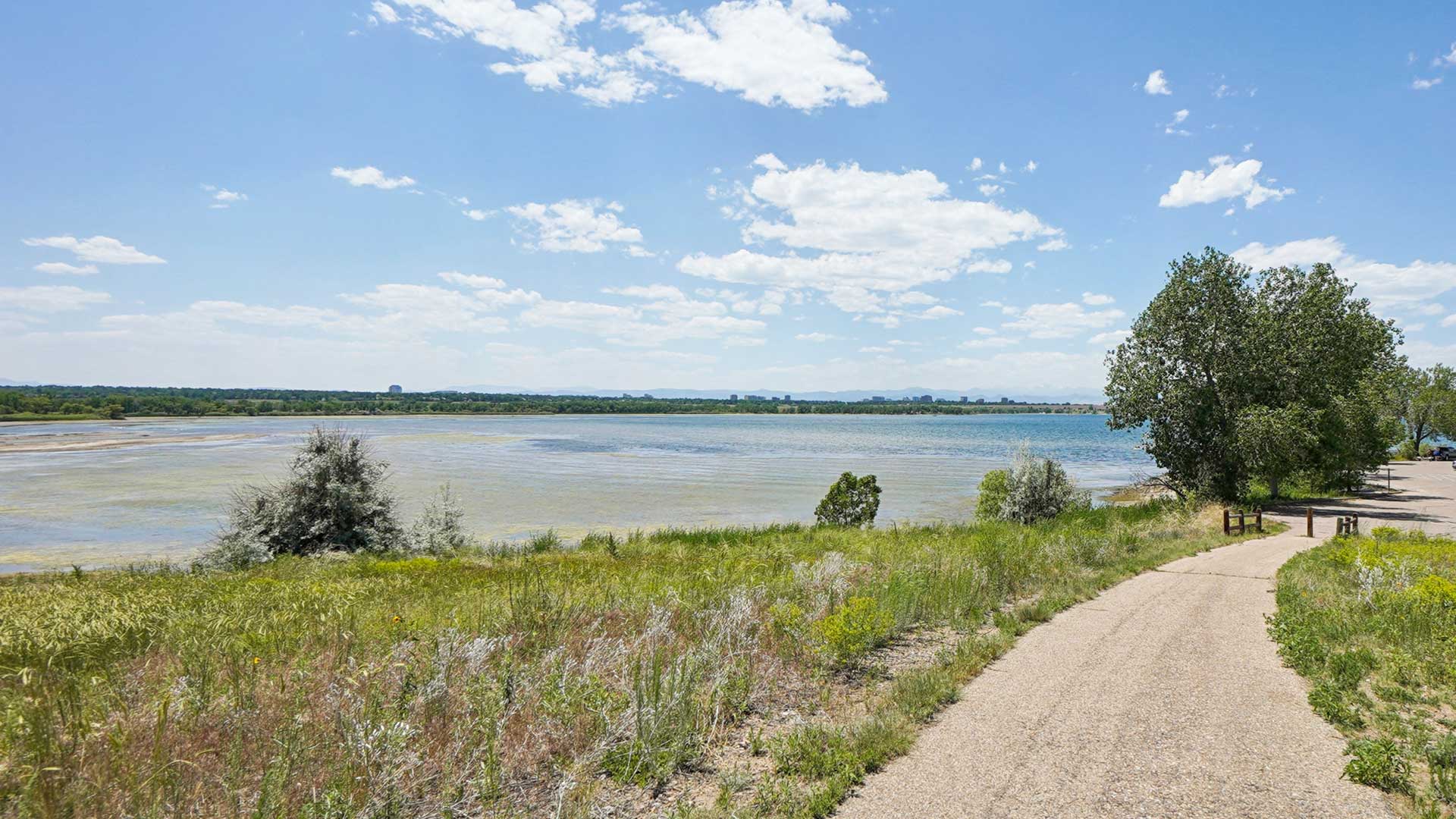 Walking trail along Cherry Creek Reservoir with lake views, open green space, and blue skies near Tempo at Nine Mile apartments.
